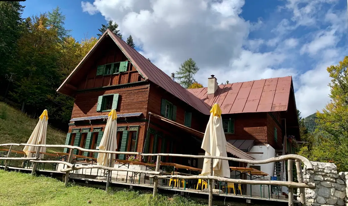 Dřevěná horská chata s terasou, stoly a slunečníky na okraji lesa