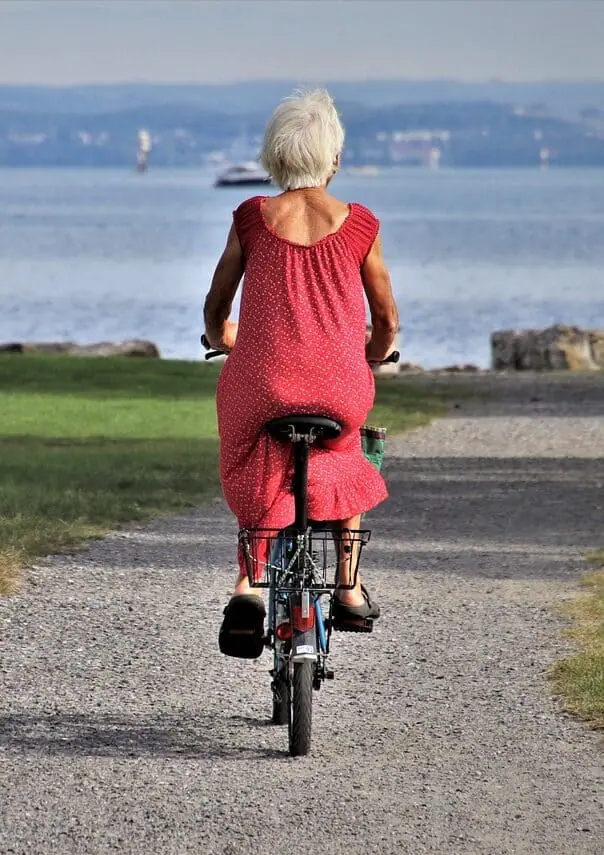Starší žena jedoucí na kole po promenádě v Limone sul Garda, symbol zdravého a aktivního života místních obyvatel.
