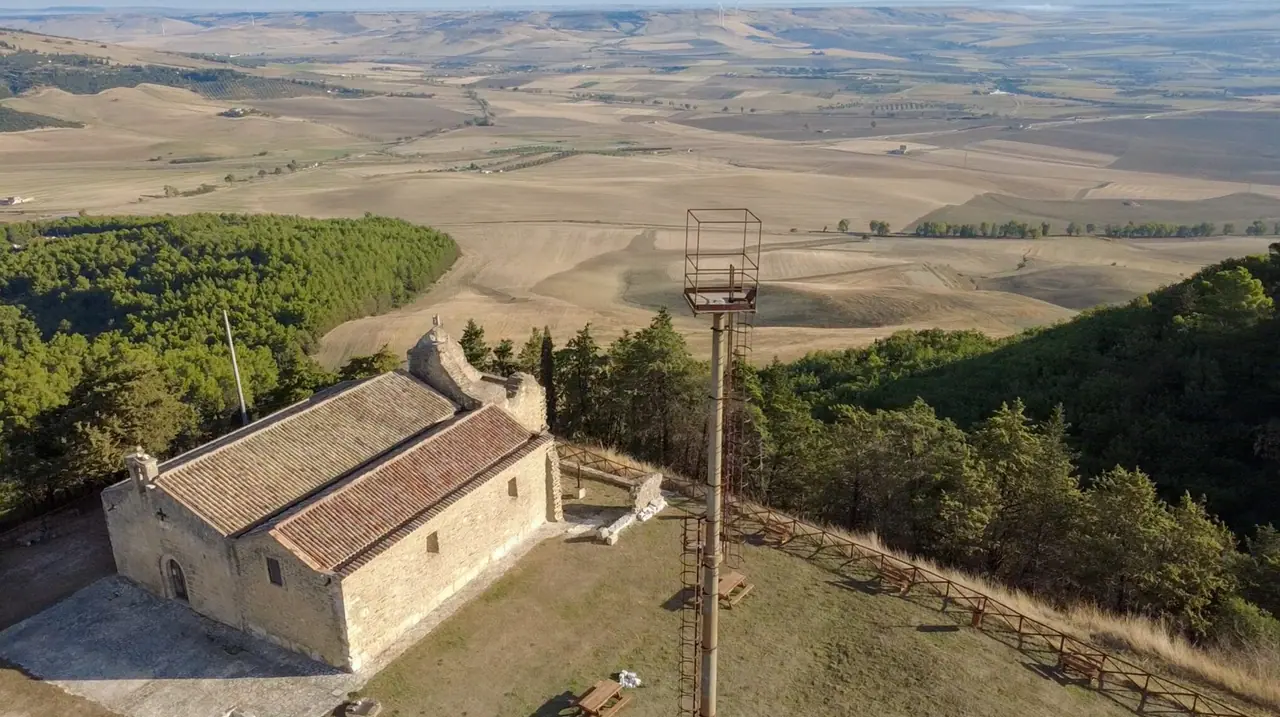 Kovový stožár u kostela San Salvatore s výhledem na zvlněnou krajinu jižní Itálie