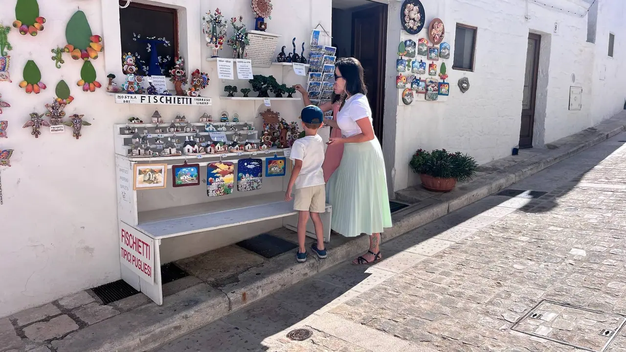 Monča s Filípkem si prohlížejí tradiční keramické fischietti píšťalky na stánku před bílými trulli domky v Alberobello