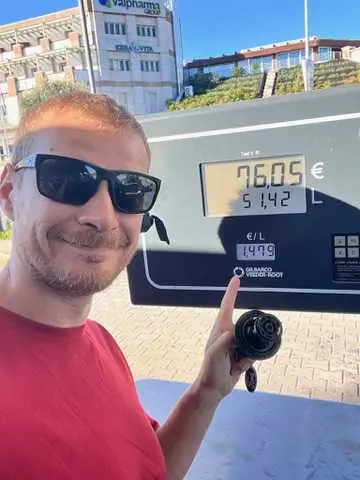 Muž v červeném tričku a slunečních brýlích ukazuje palcem nahoru u benzínové pumpy s cenou 96,05 euro za natankovaných 51,42 litrů