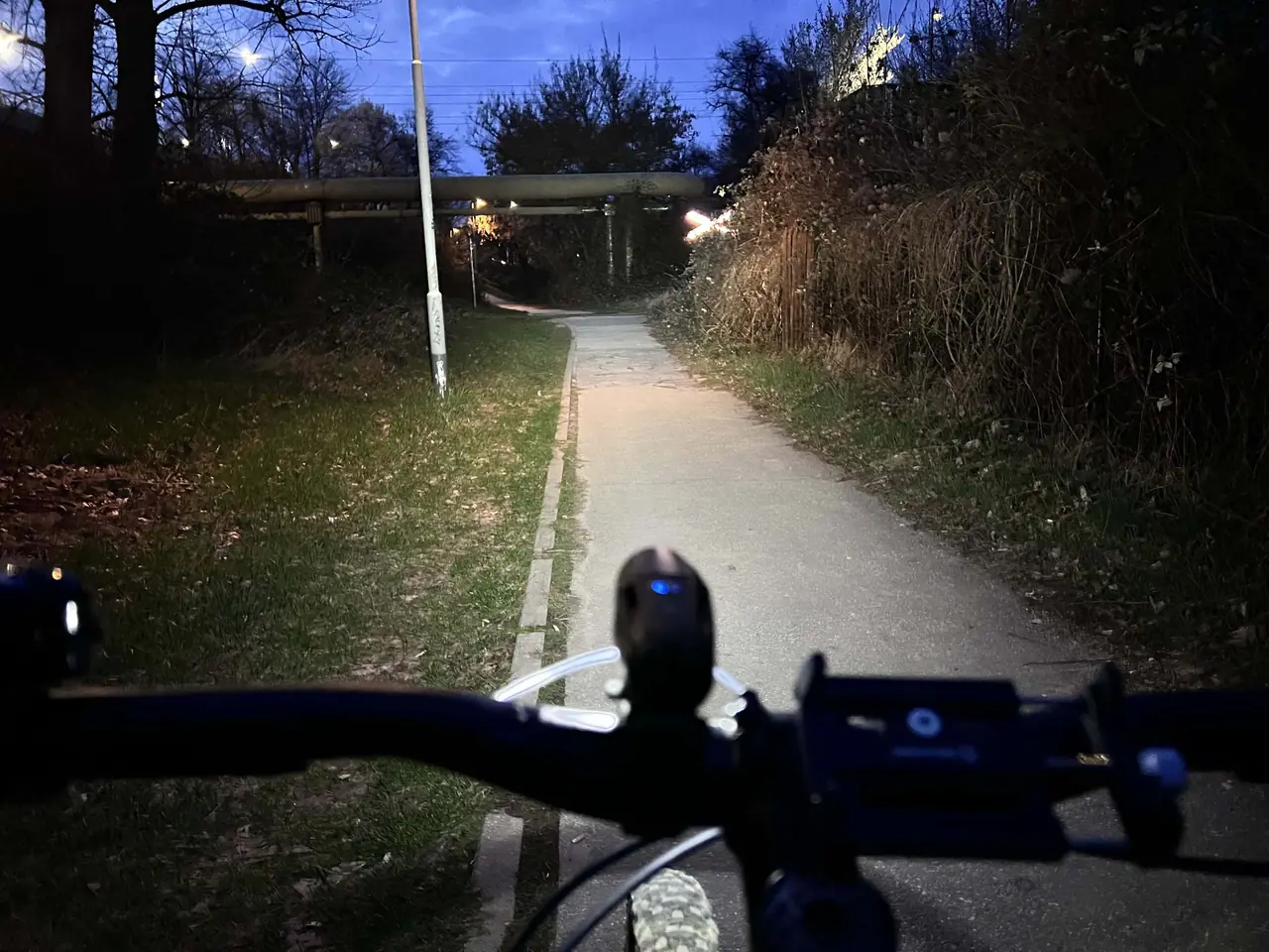 Pohled z řídítek kola na osvětlenou cyklostezku za soumraku s LED světlem Moon Meteor X Auto Pro