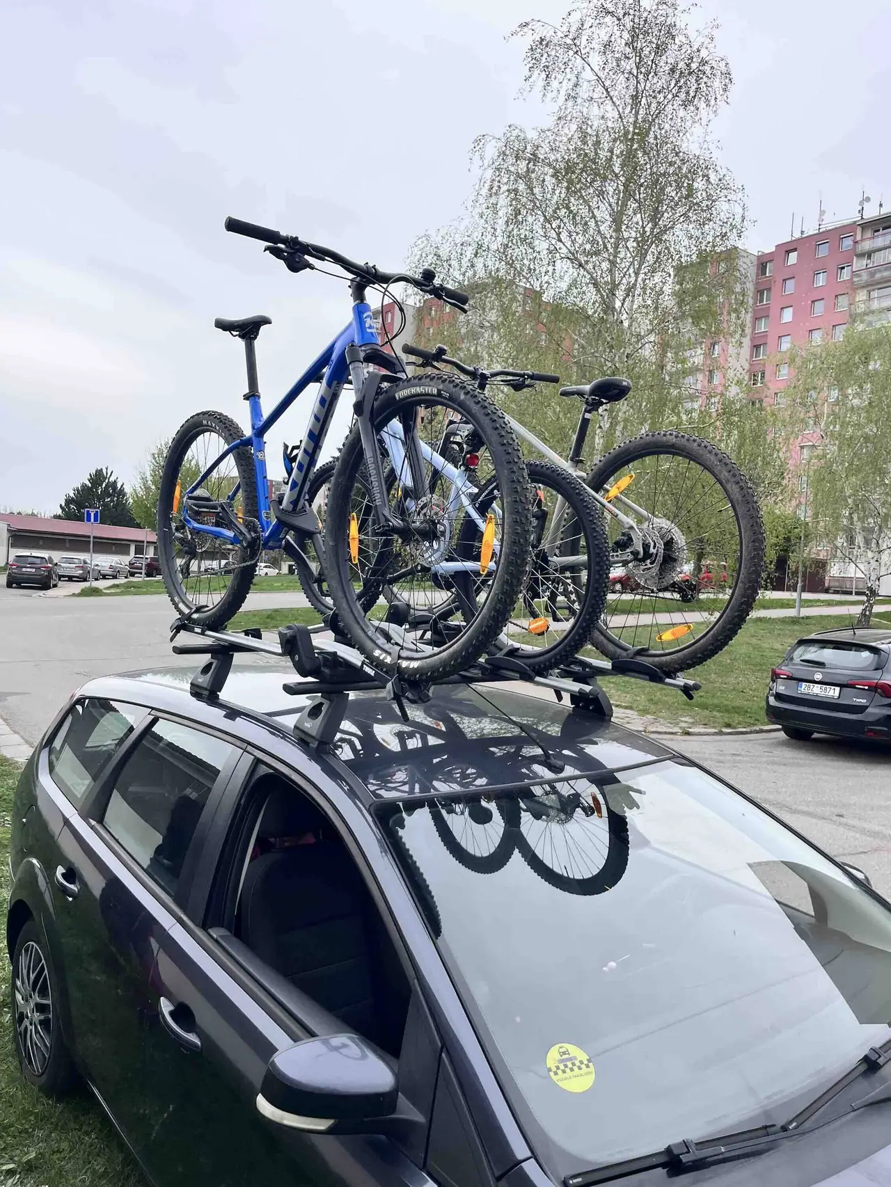Čtyři horská kola na nosič Thule VeloCompact připevněném k našemu autu na parkovišti v brněnském sídlišti
