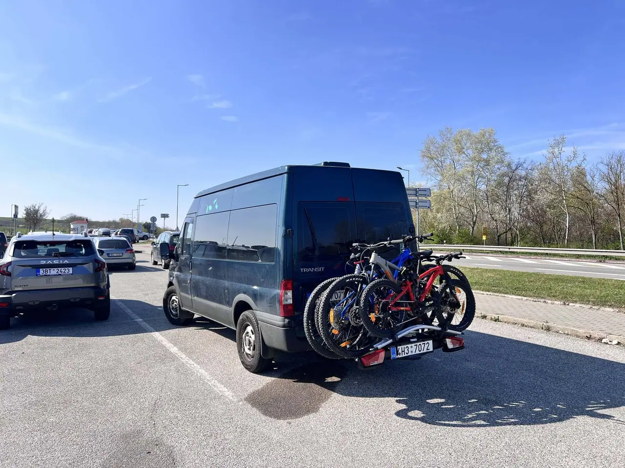 Náš šedý Ford Transit s nosičem Thule na tažném háku se čtyřmi koly stojí v dopravní zácpě na dálnici