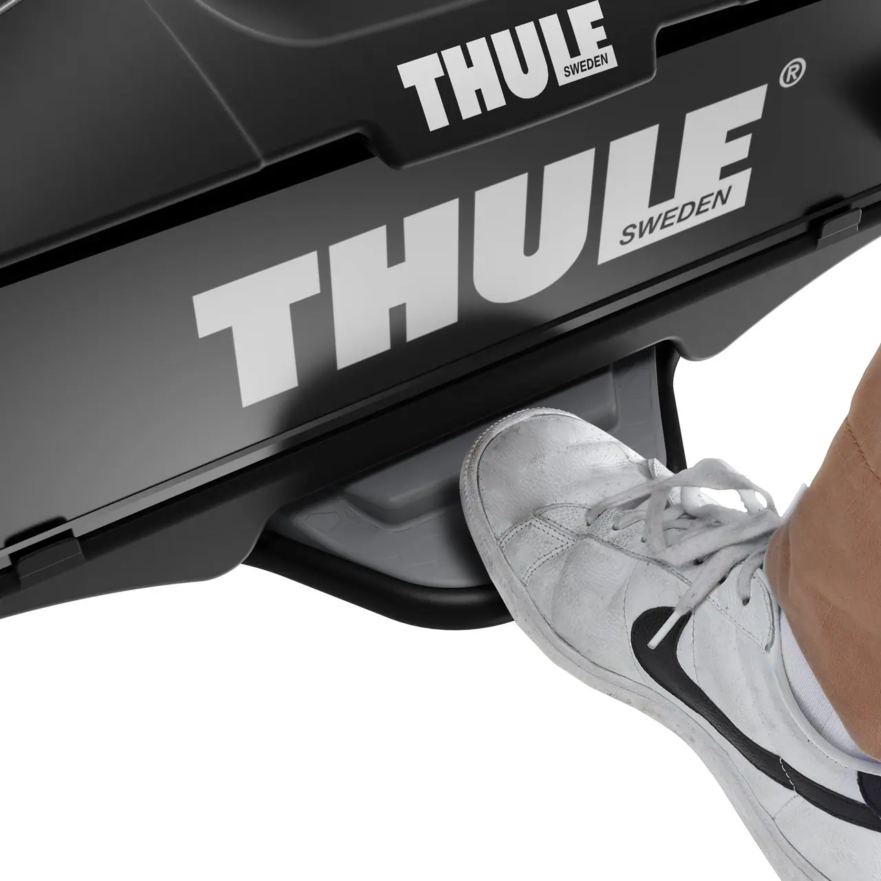 Detail nosiče kol Thule VeloCompact na tažném zařízení s plastovým nášlapem, kam právě vstupuje noha v šedé botě