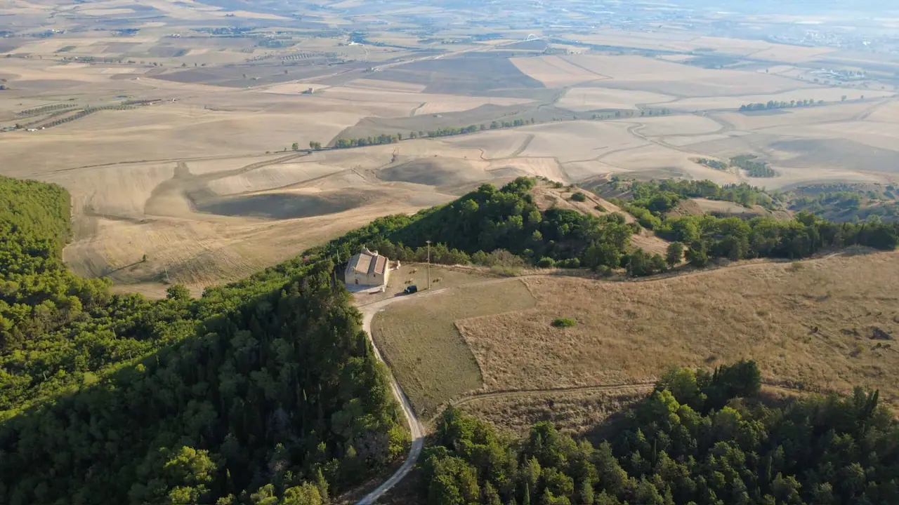 Kostel San Salvatore v oblasti Timmari obklopený zvlněnou krajinou a poli při pohledu z výšky