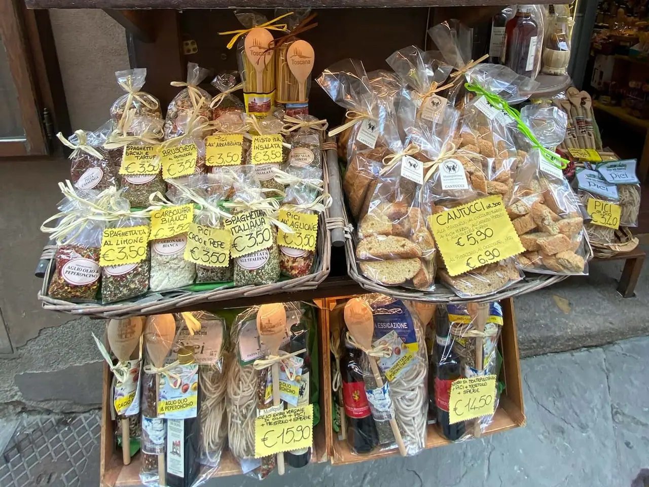 Regál s místními produkty v Montepulcianu - domácí těstoviny, omáčky, olivový olej a cantucci se žlutými cenovkami v eurech