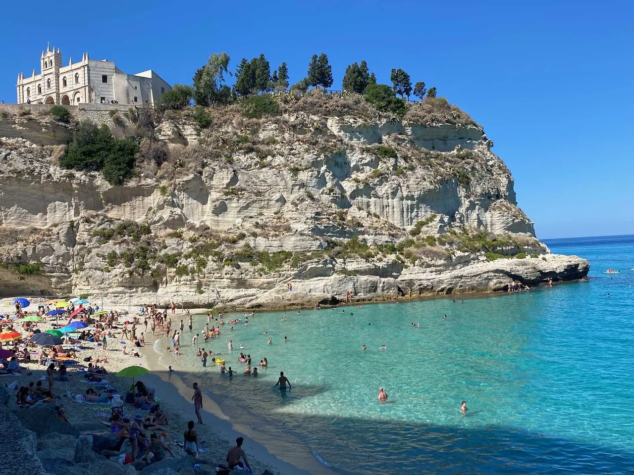 Pláž v Tropea s čistým tyrkysovým mořem, bílými útesy a historickým kostelem Santa Maria dell'Isola na vrcholu skály