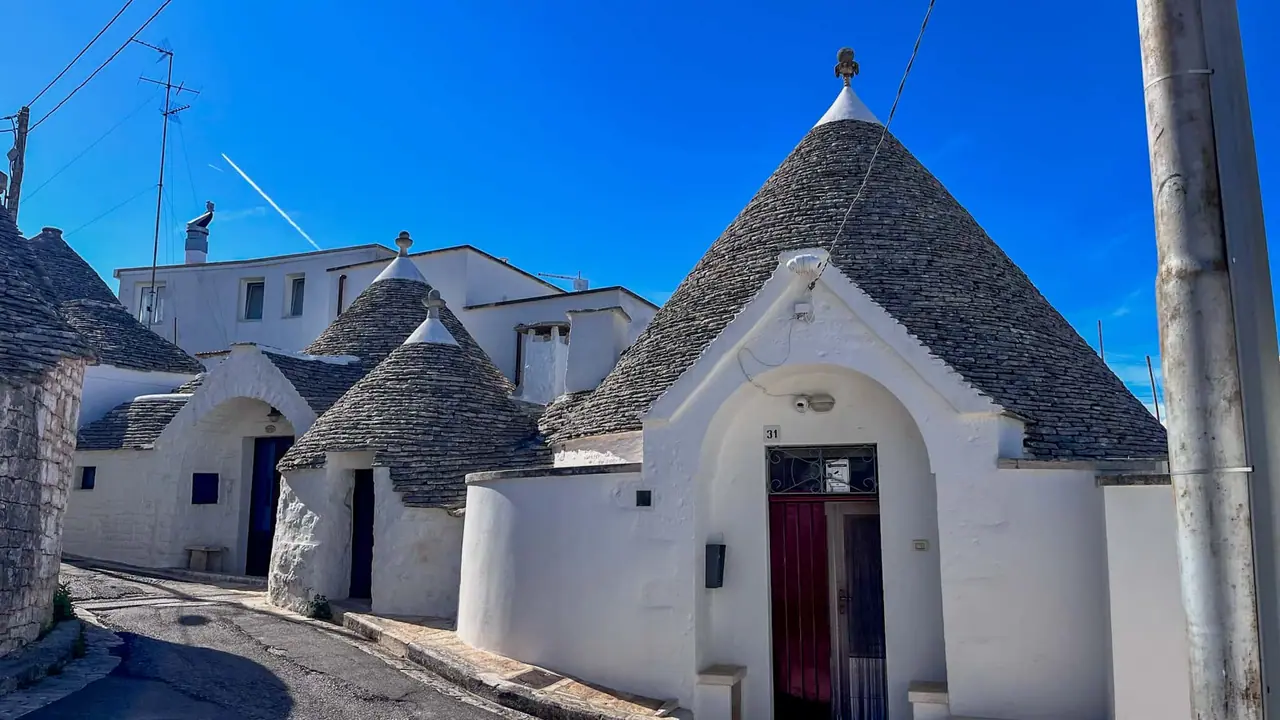 Typické bílé trulli domečky s kuželovitými kamennými střechami v úzké dlážděné uličce historického centra Alberobella