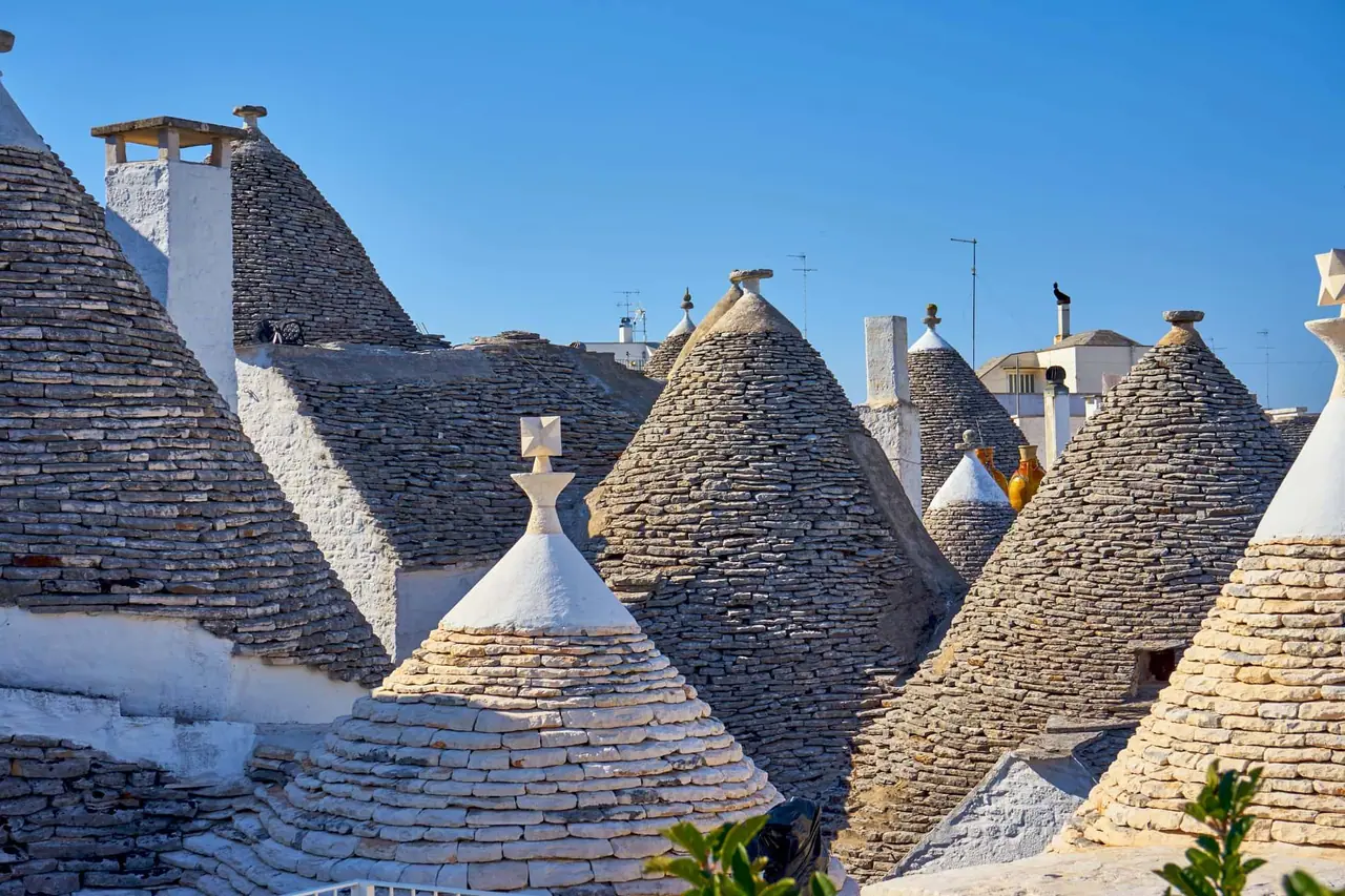 Kamenné kužely tradičních trulli domků v Alberobello s bílými komíny a šedými střešními taškami pod modrým nebem