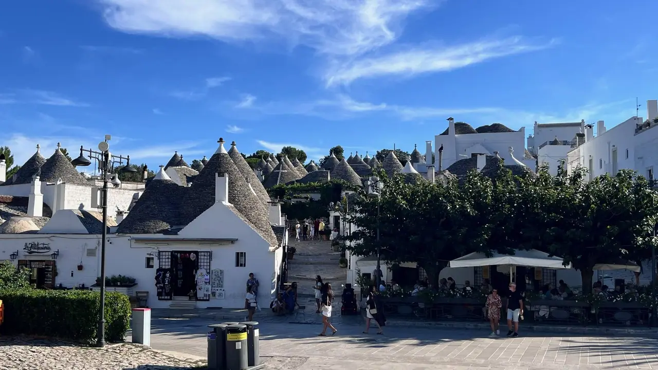 Turisté procházejí mezi tradičními trulli domky s kamenými kužely v historickém centru města Alberobello v Apulii