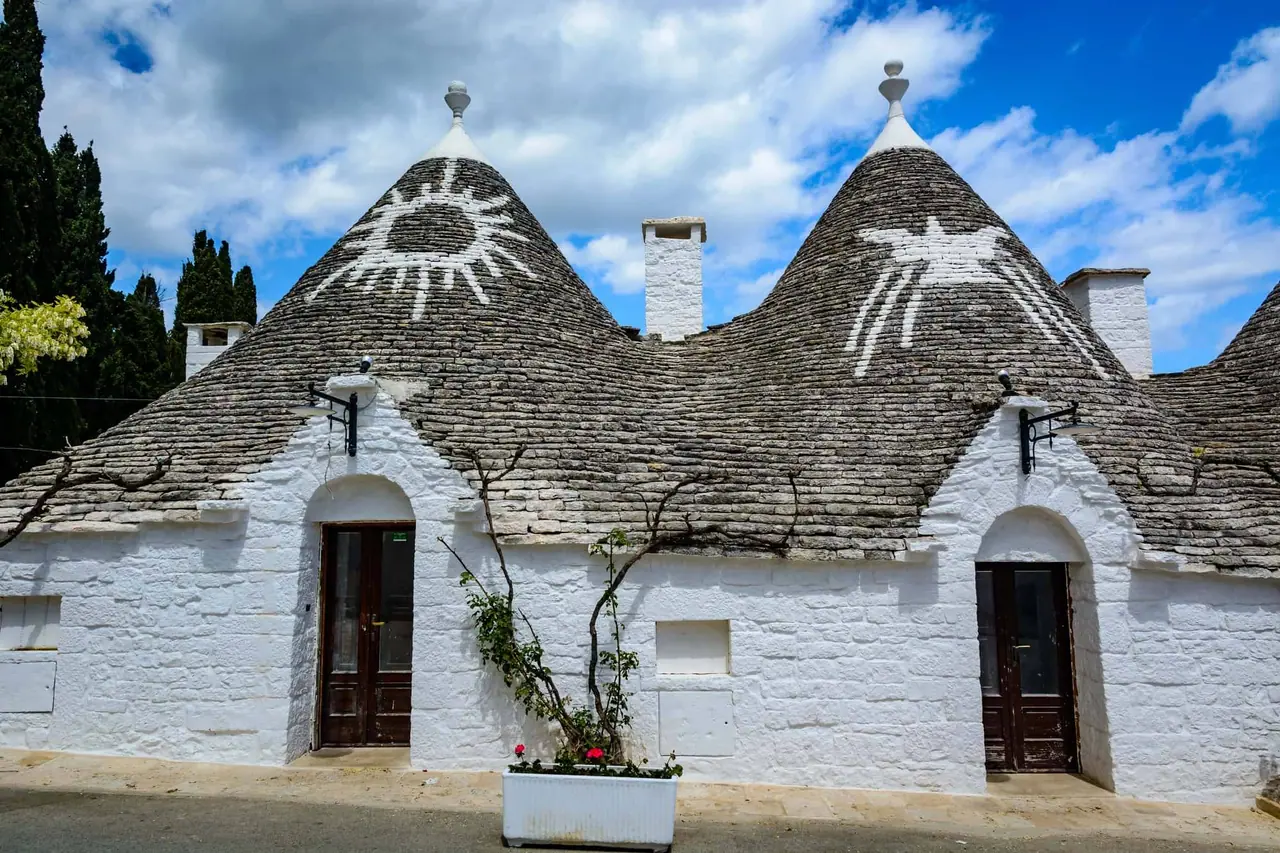 Bílé trulli domky s kuželovitými kamennými střechami a symboly v Alberobello, které jsme navštívili během naší cesty Puglia
