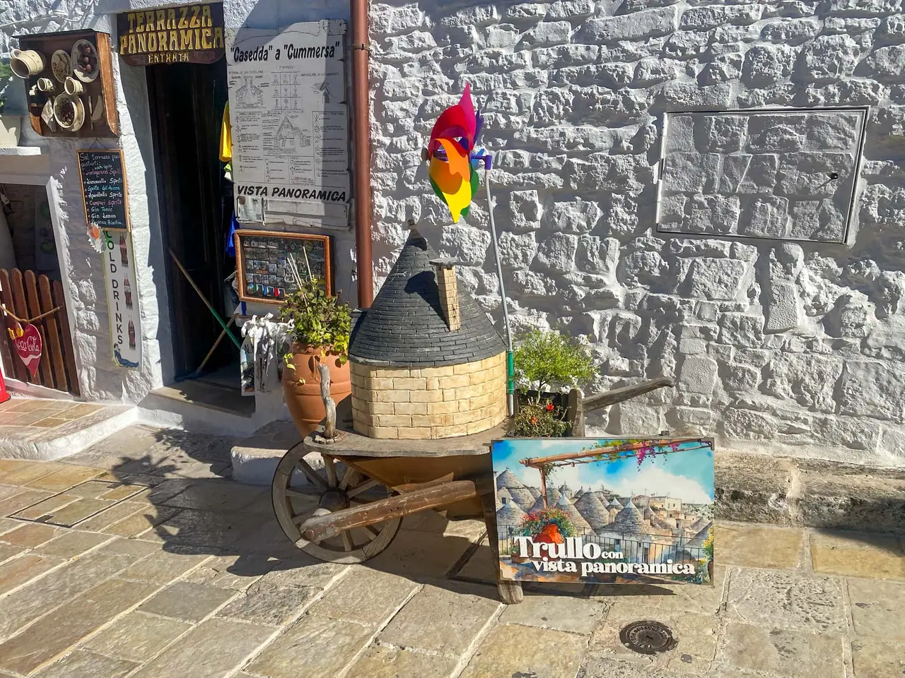 Propagační stánek s miniaturním trullo domečkem a reklamou na Vista Panoramica u historického centra Alberobella