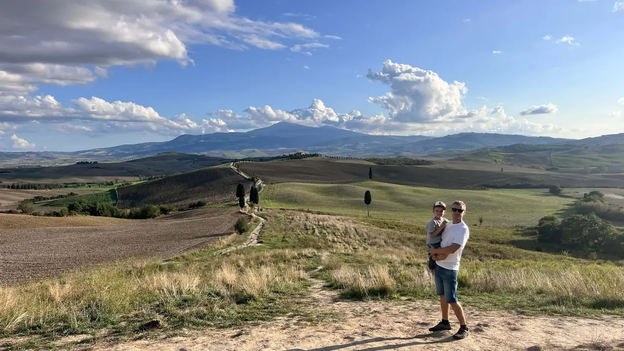 Táta s dítětem v náručí stojí na cestě mezi cypřiši v toskánském Val d'Orcia, kde se natáčel film Gladiátor