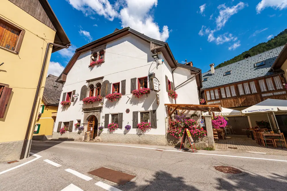 Bílý alpský dům s truhlíky muškátů a terasou restaurace ve Valbruně