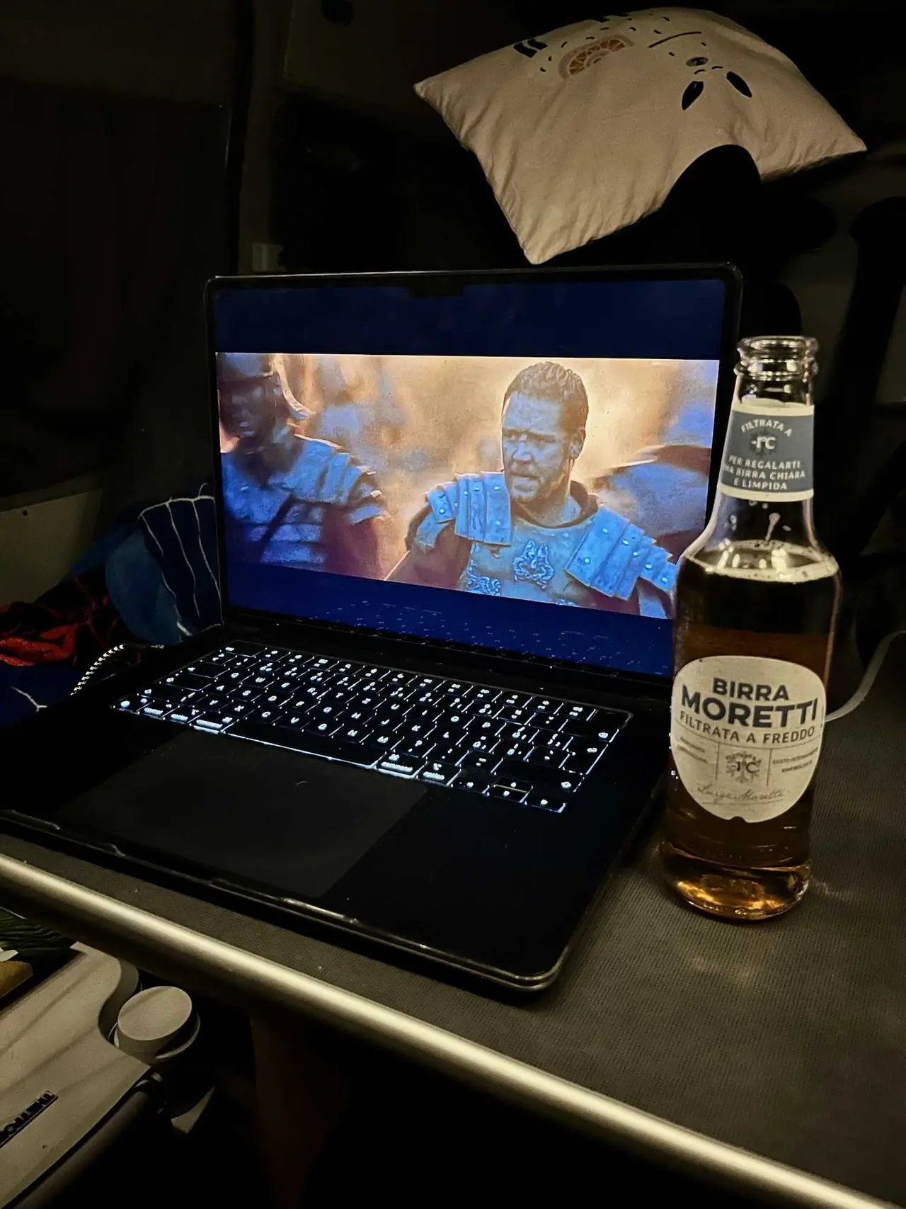 Otevřený notebook s filmem Gladiátor na obrazovce a lahev italského piva Birra Moretti na stole v kempu