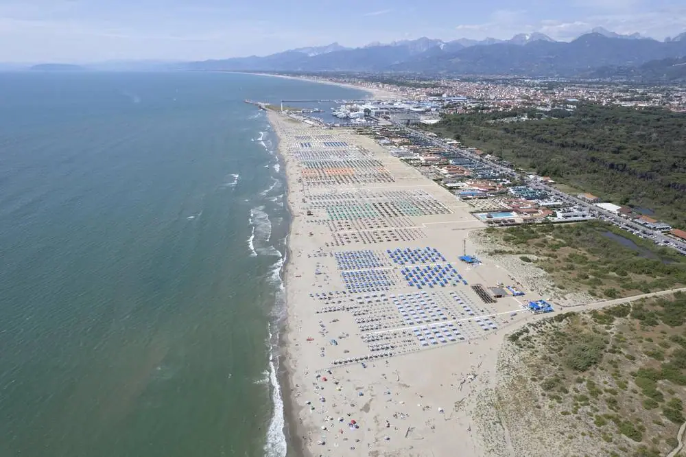Letecký pohled na pláž Viareggio v Toskánsku s řadami modrých slunečníků podél písčitého pobřeží Tyrhénského moře
