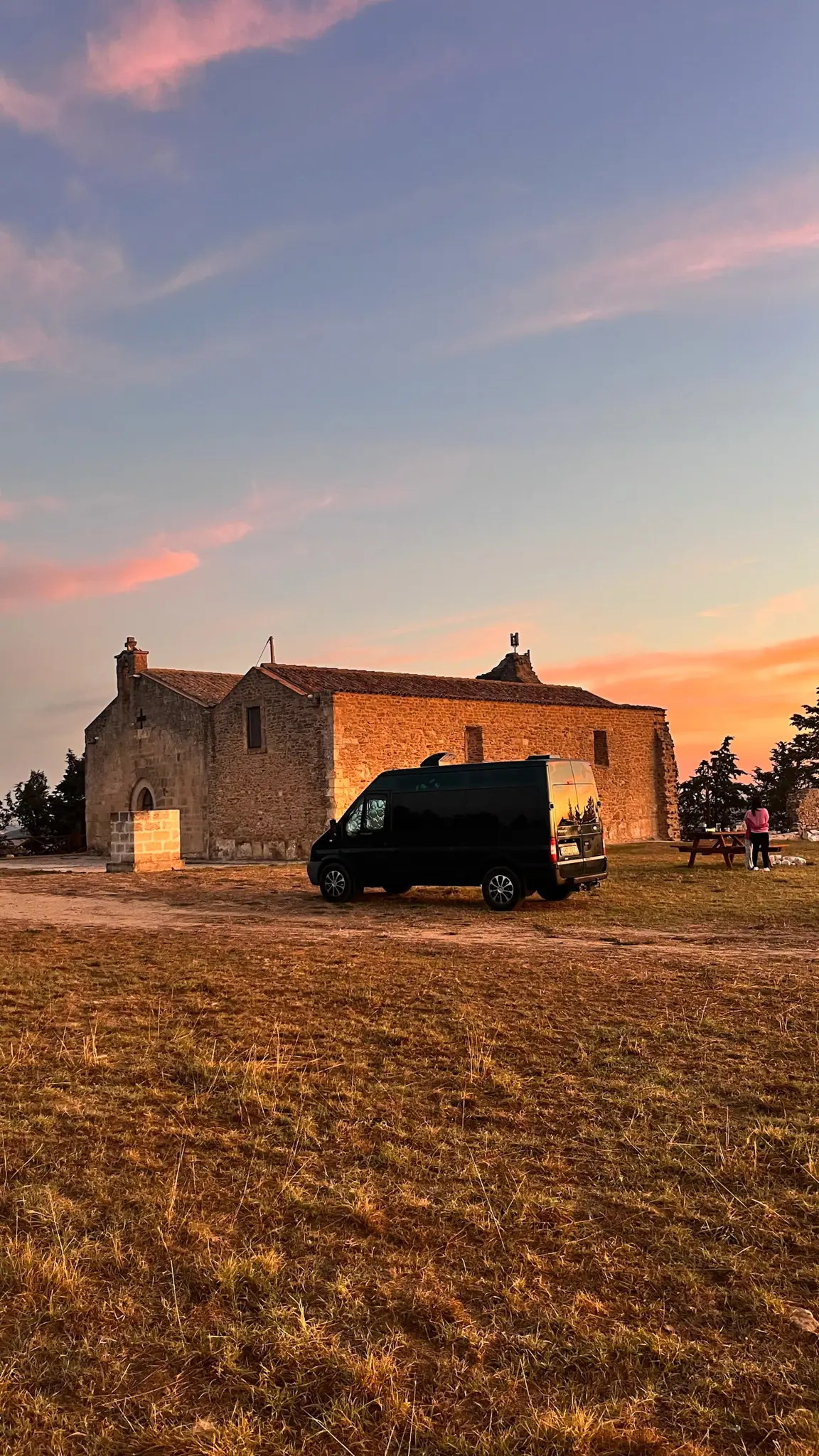 Kaple San Salvatore za svítání s černým obytným vozem Transit v popředí