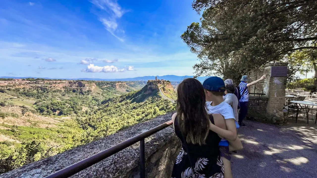 Turisté pozorují Civita di Bagnoregio z panoramatické vyhlídky s výhledem na město a okolní kaňon.